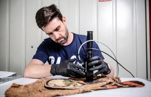 Man in blue shirt and black gloves holding device over an artifact